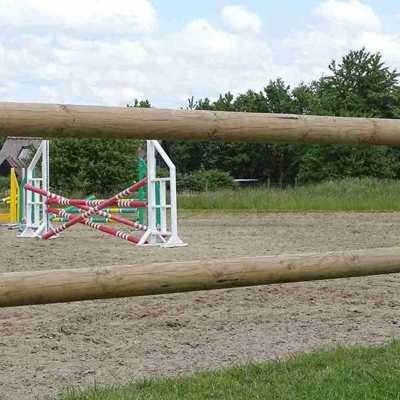 Die Sprünge eines Reitplatzes sind zwischen den Latten des Holzzauns zu erkennen.