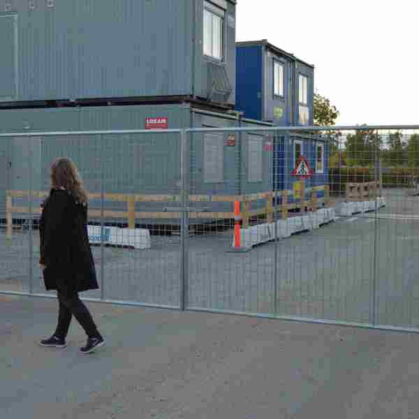 Eine Frau geht vor einem leichtgewichtigen Tor, das auf einer Baustelle montiert ist.