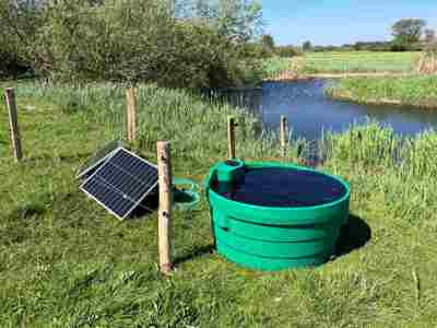 Solarbetriebene Feldpumpe mit Solarpanel und Wassertrog an einem Bach auf einer Wiese