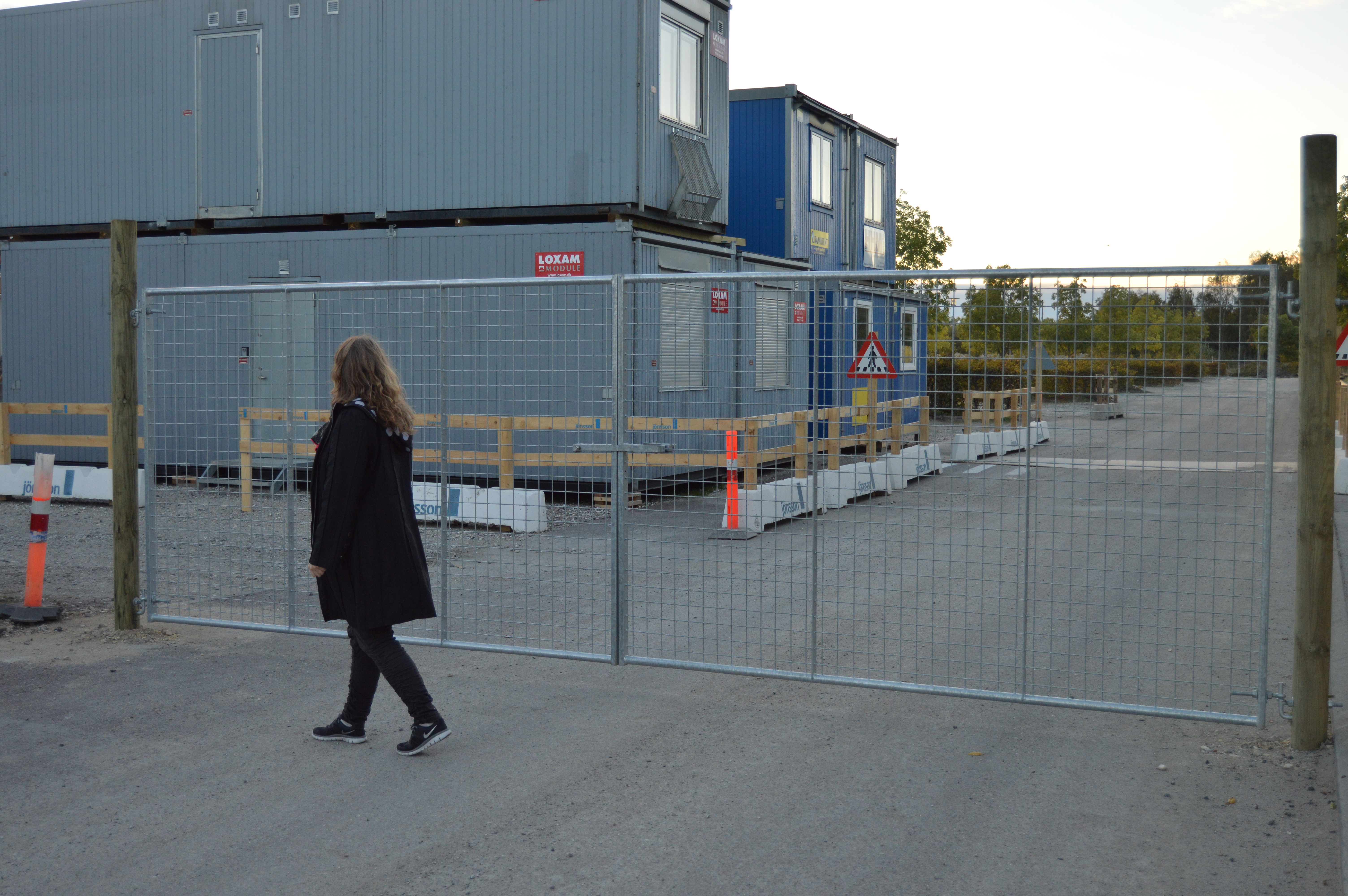 Eine Frau geht vor einem leichtgewichtigen Tor, das auf einer Baustelle montiert ist.