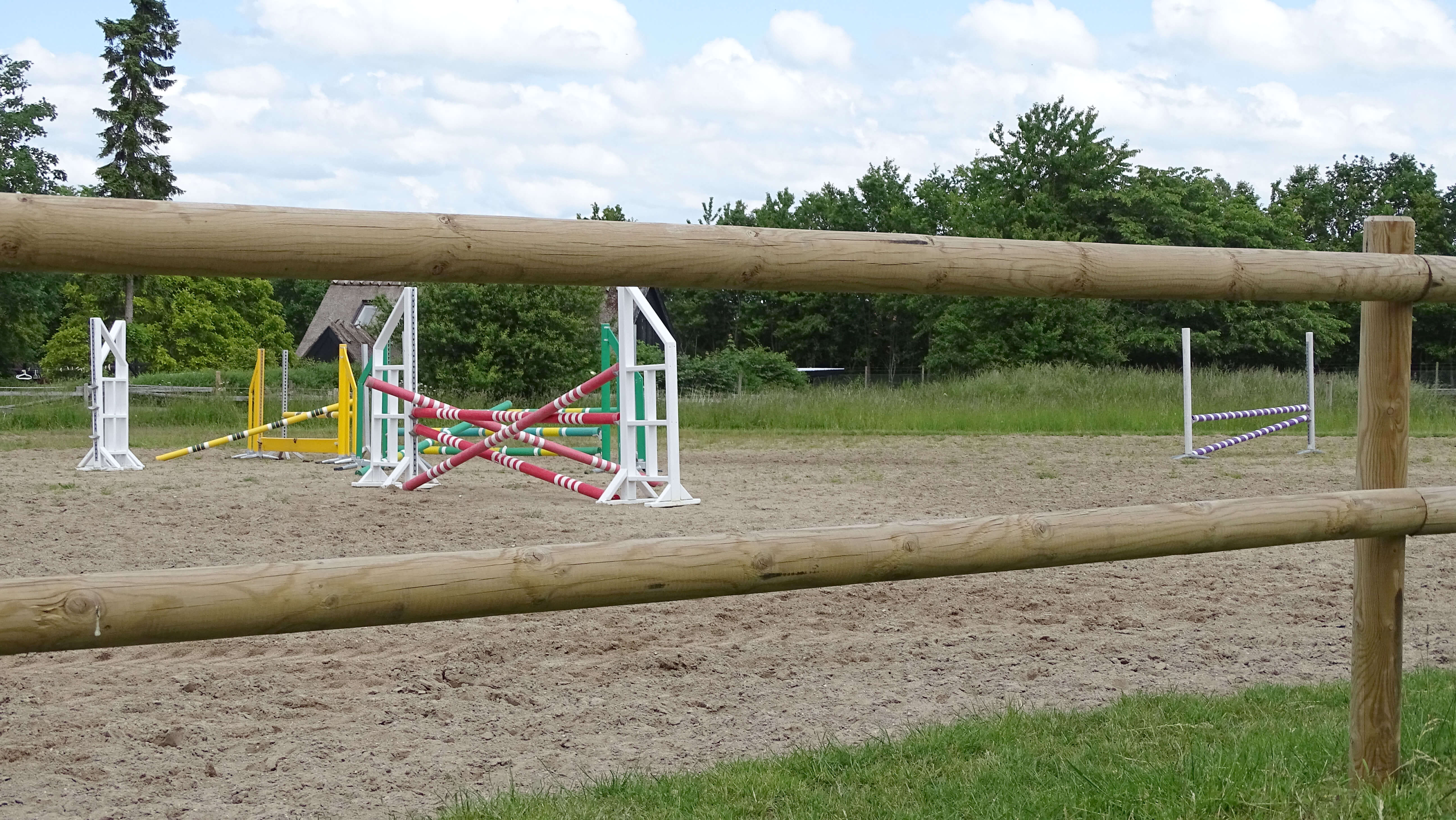 Die Sprünge eines Reitplatzes sind zwischen den Latten des Holzzauns zu erkennen.