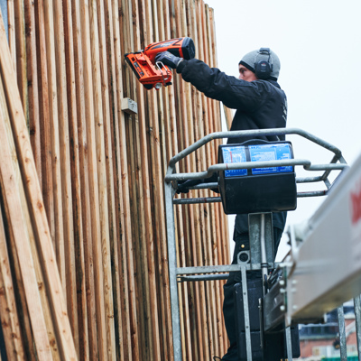 Monteur befestigt Holzverkleidung an einem hohen Holzzaun von einer Hebebühne aus.