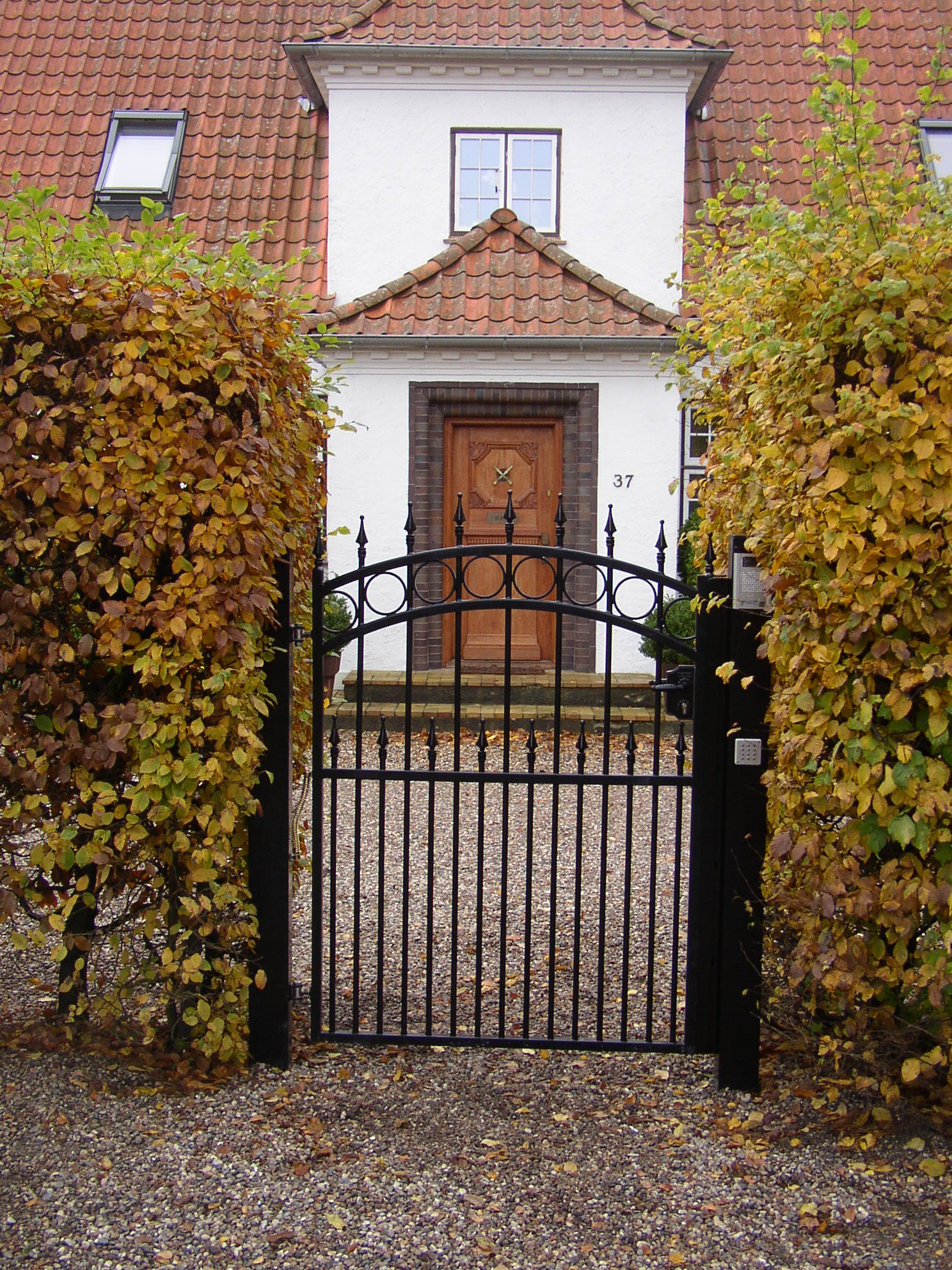 Ein schwarzes schmiedeeisernes Fußgängertor ist zwischen zwei Büschen montiert, die den Eingang zu einem Haus bilden.