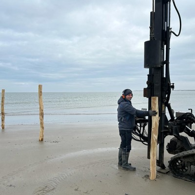 Monteur setzt Holzpfosten mit einer Maschine an einem Strand an der Küste.