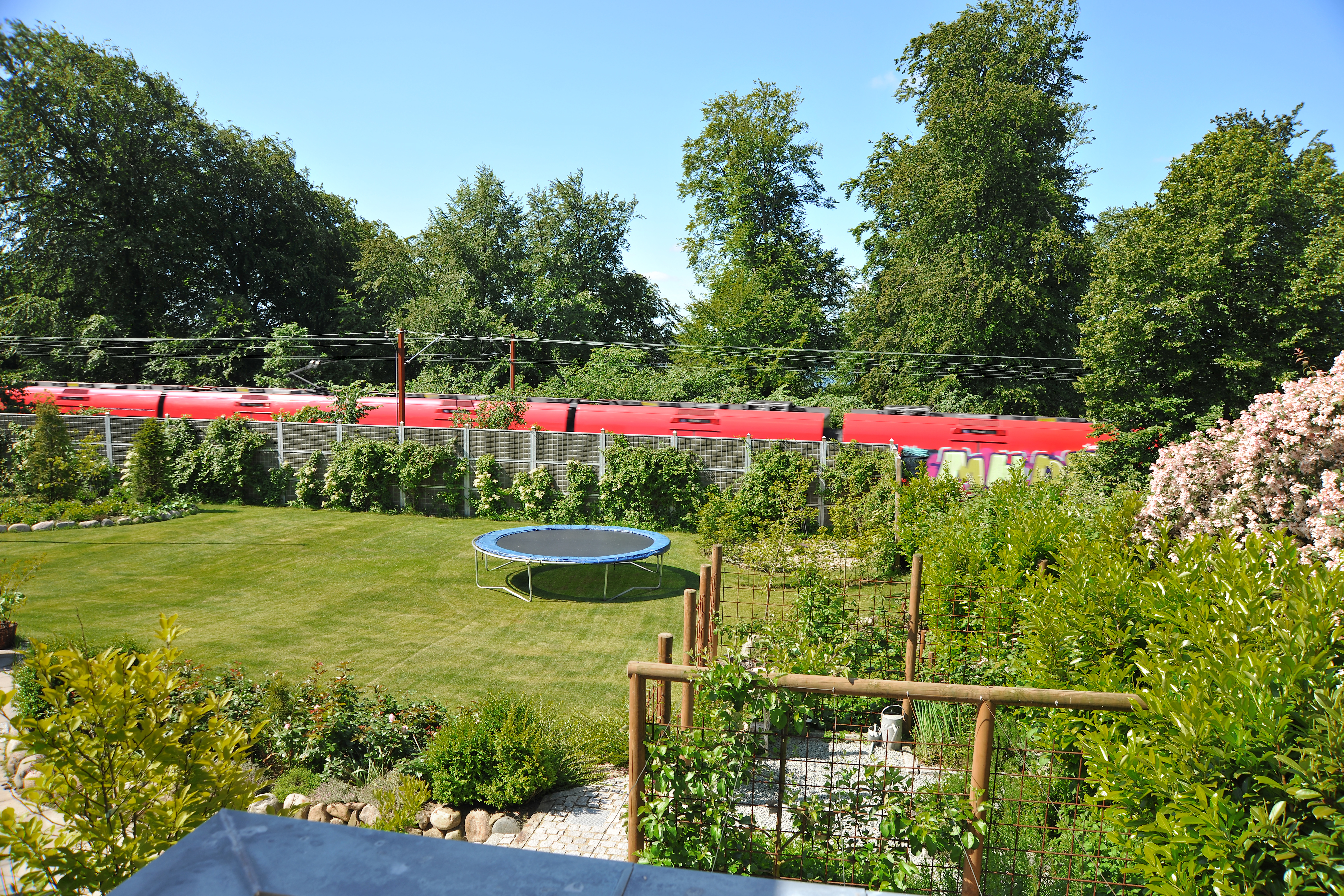 Ein Noistop® Steel-Lärmschutzzaun von Poda Zaun mit Bepflanzung in einem Garten, um den Lärm einer direkt neben dem Garten verlaufenden Bahnstrecke abzuschirmen