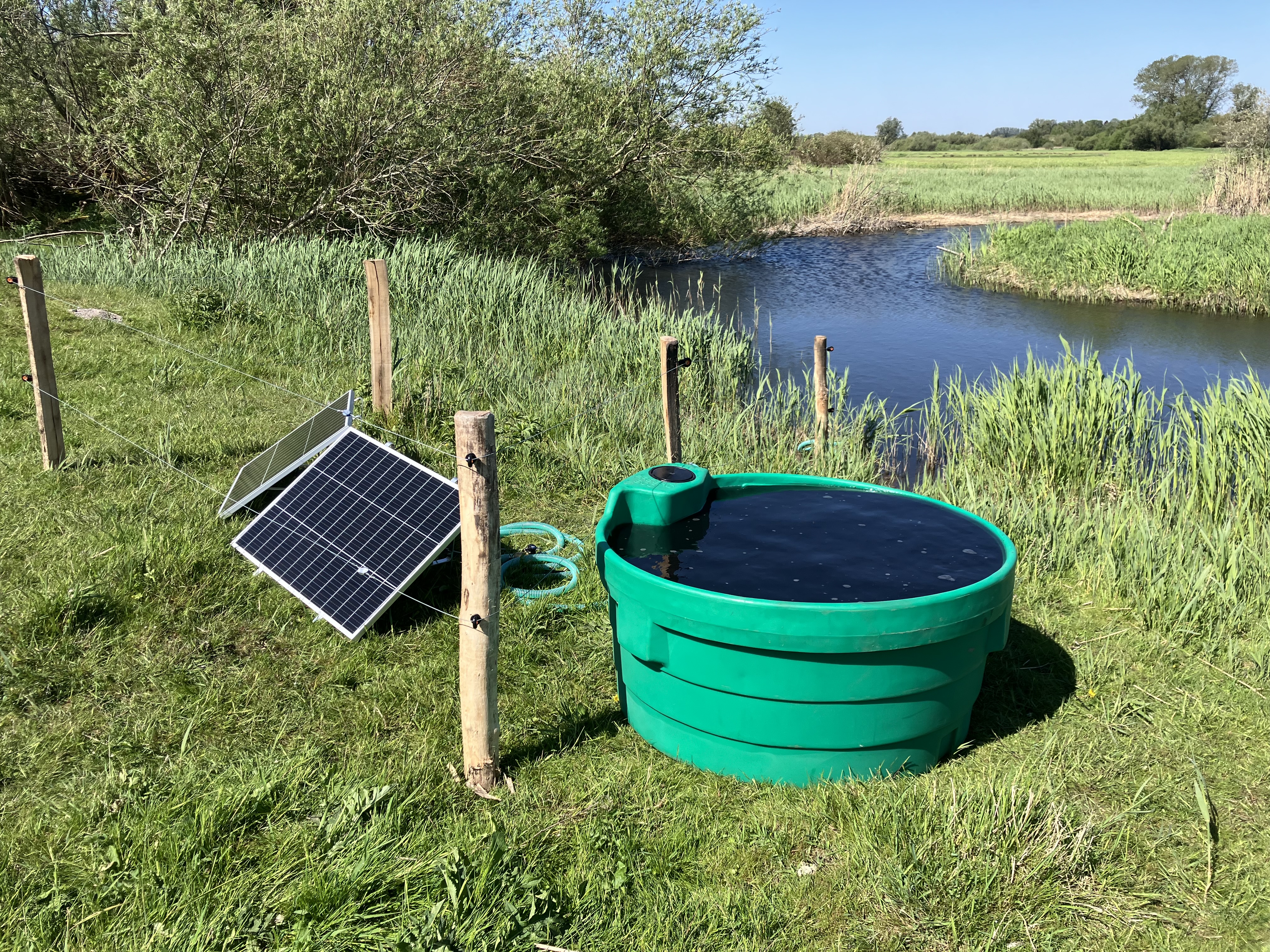 Solarbetriebene Feldpumpe mit Solarpanel und Wassertrog an einem Bach auf einer Wiese