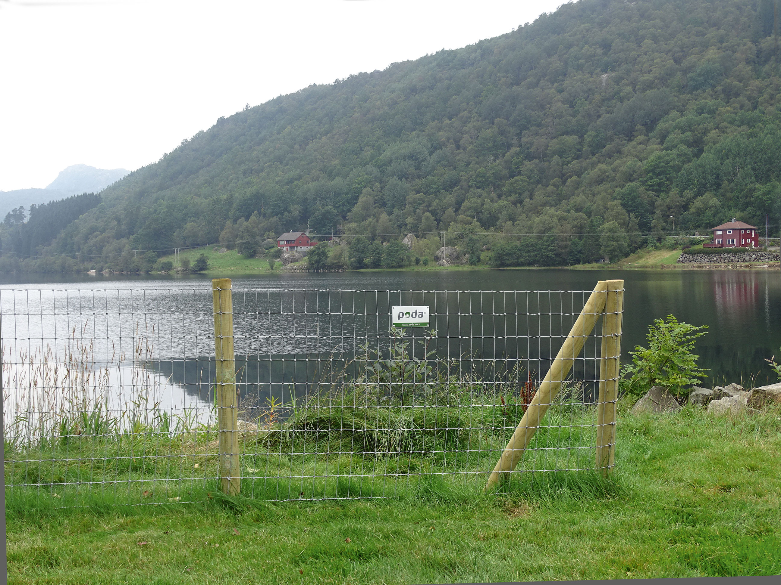 Zaunende an einem Multinet-Zaun. Im Hintergrund sind ein See und Häuser zu sehen