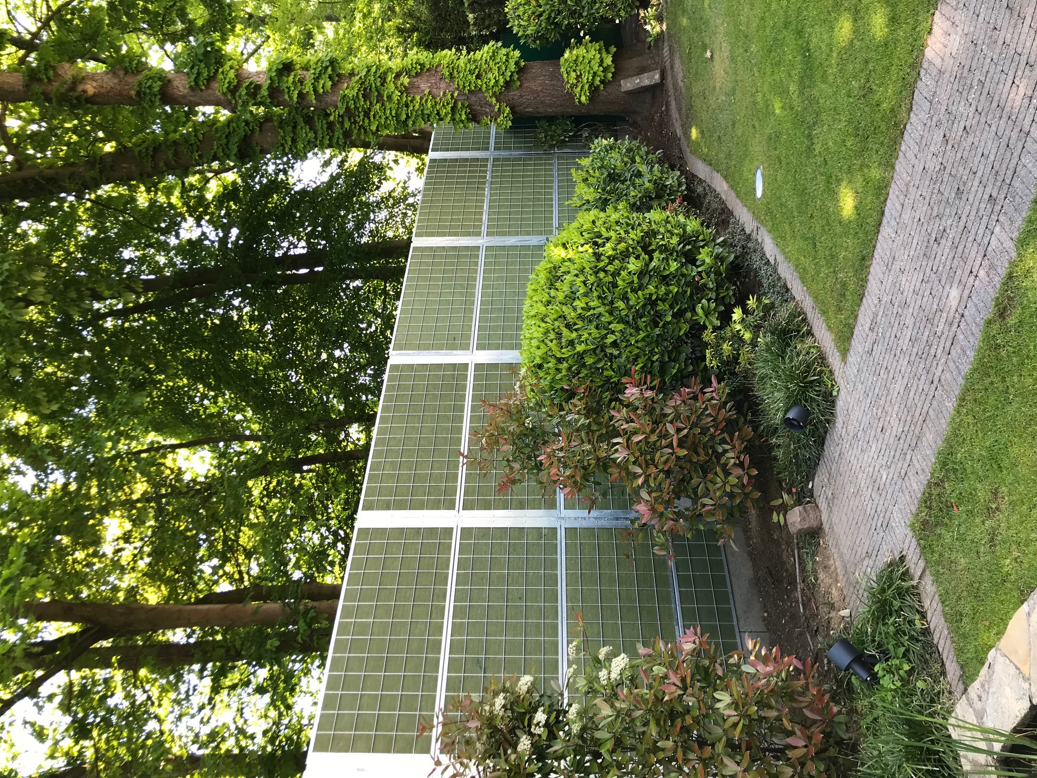 Ein Noistop® Steel-Lärmschutzzaun von Poda Zaun in einem von Sträuchern und Bäumen umgebenen Garten