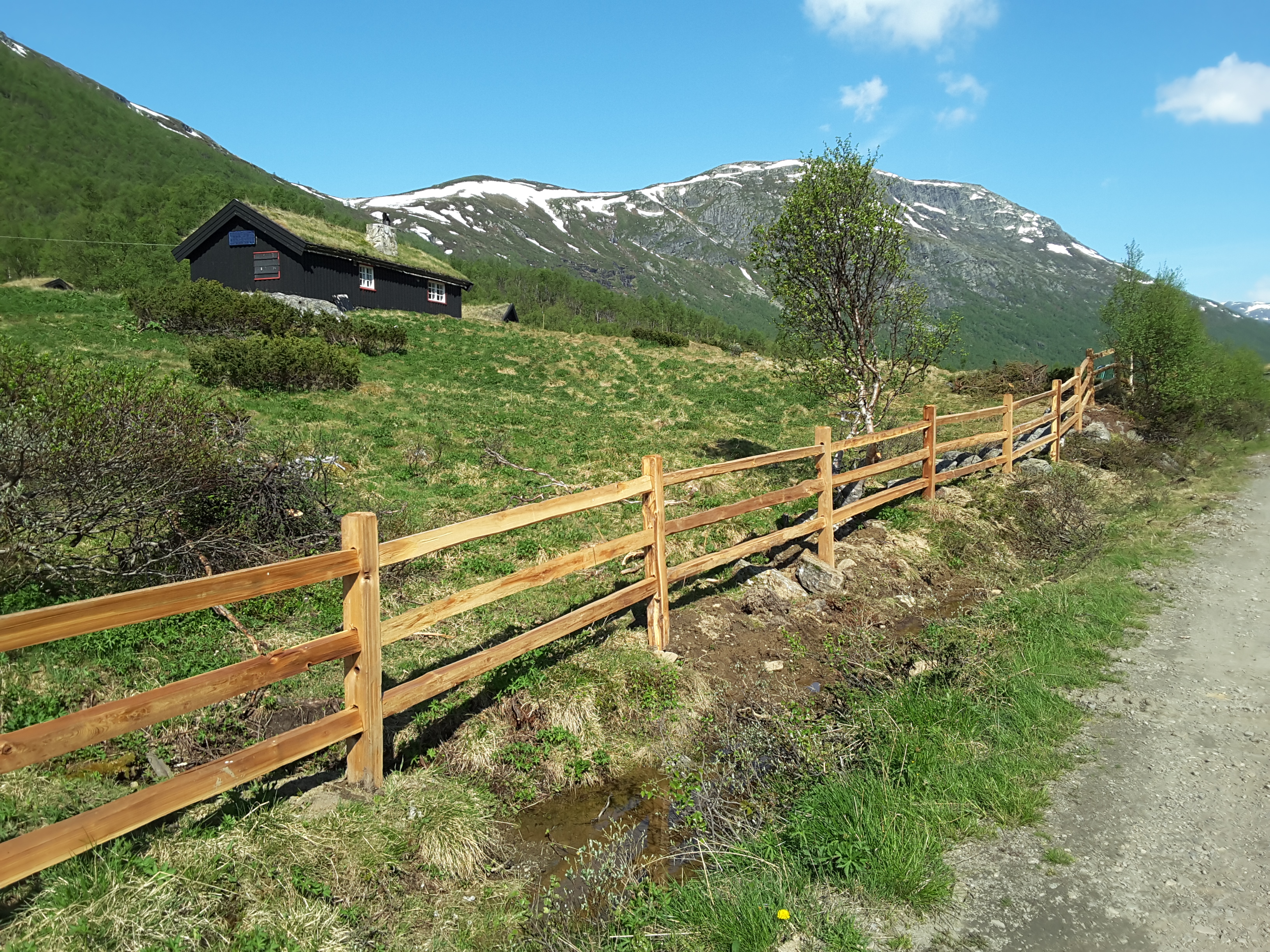 Ein rustikaler Lattenzaun aus Zedernholz begrenzt ein Naturgrundstück mit einer Hütte in einer Bergregion.