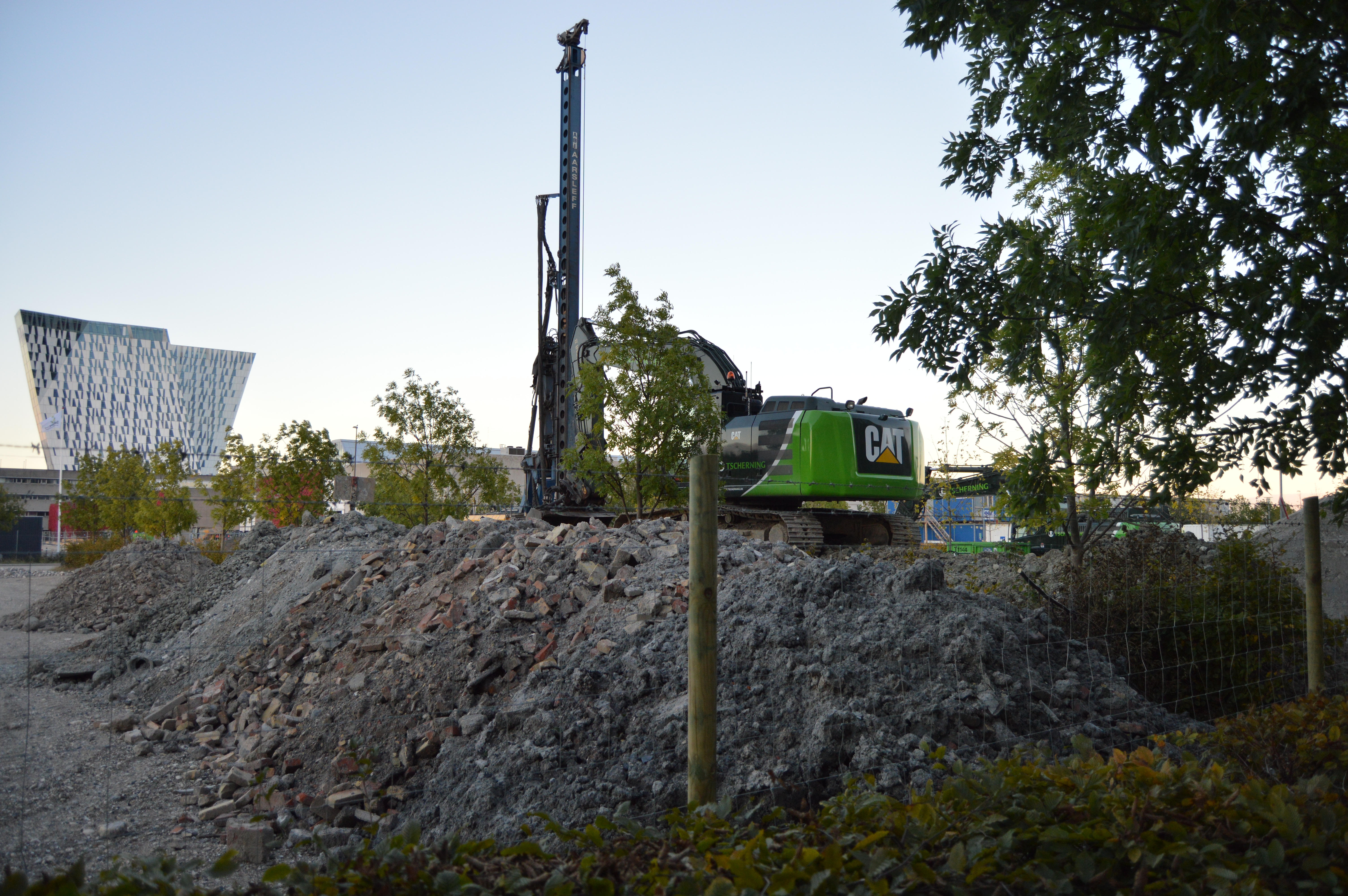 Eine grüne CAT-Maschine ist auf einem Schotterhaufen abgestellt. Die Maschine ist mit einem Baustellenzaun gesichert