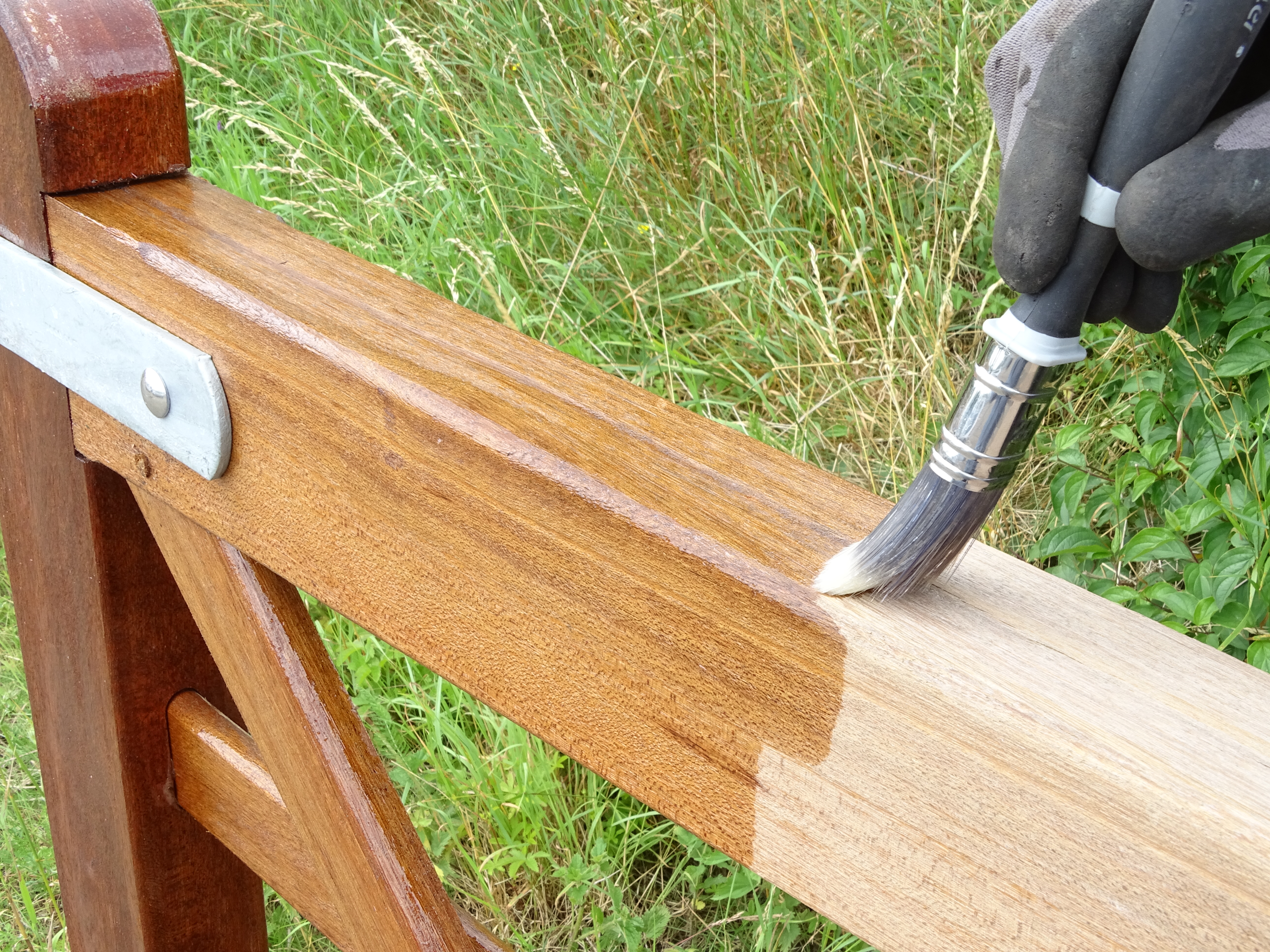 Eine Person mit Handschuhen trägt mit einem Pinsel Holzschutz auf ein Holztor auf. Das behandelte Holz erscheint dunkler als der unbehandelte Bereich.