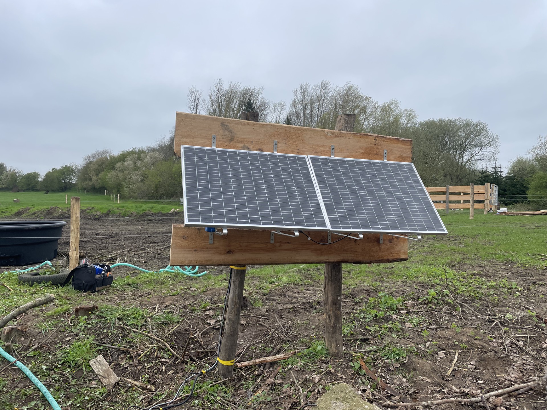 Solarbetriebene Feldpumpe mit Solarpaneelen, montiert auf einer Holzkonstruktion in einer Weide