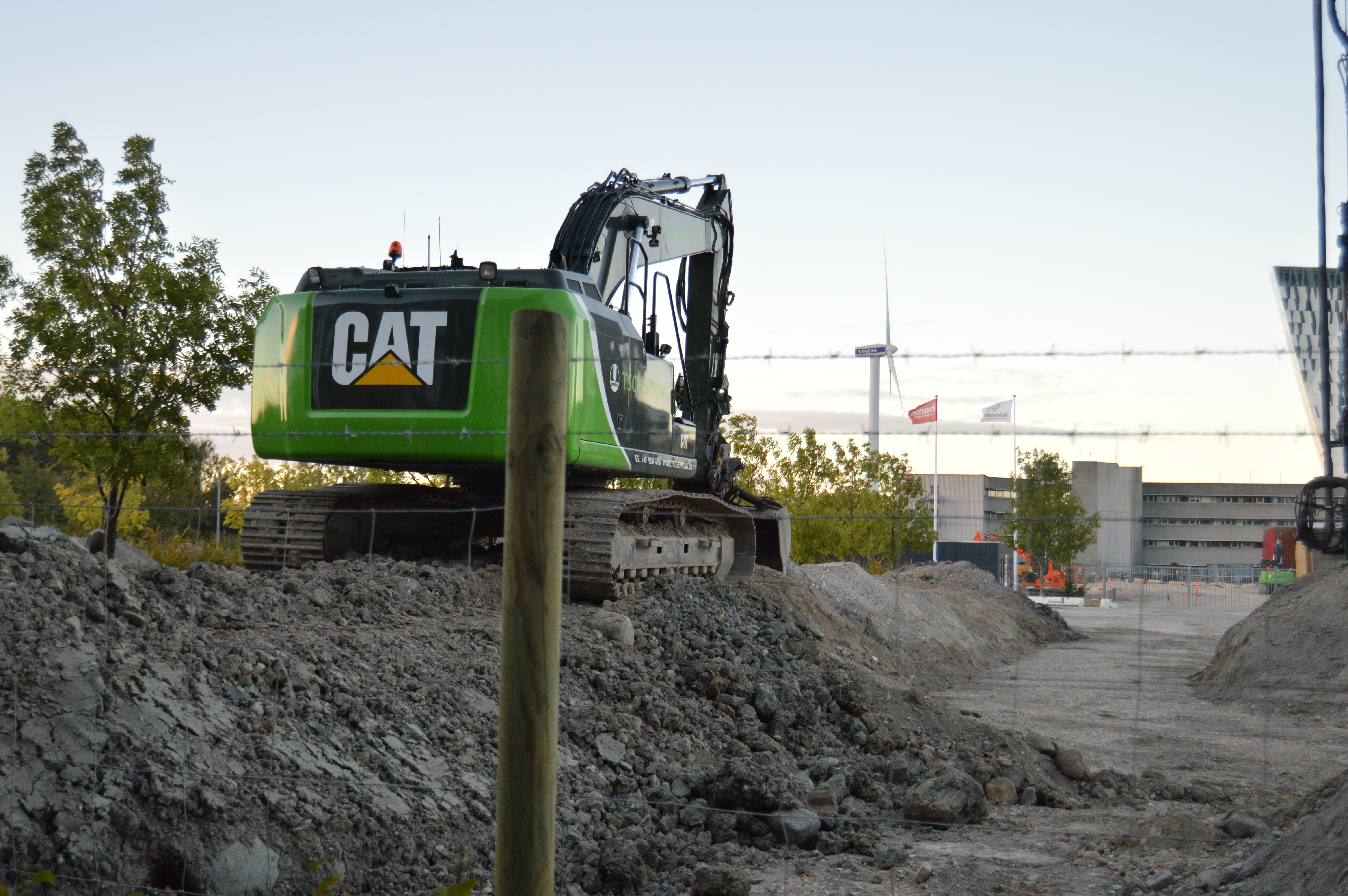 Auf einer Baustelle ist eine grüne CAT-Maschine abgestellt. Um die Sicherheit auf der Baustelle zu erhöhen, wurde ein Baustellenzaun errichtet