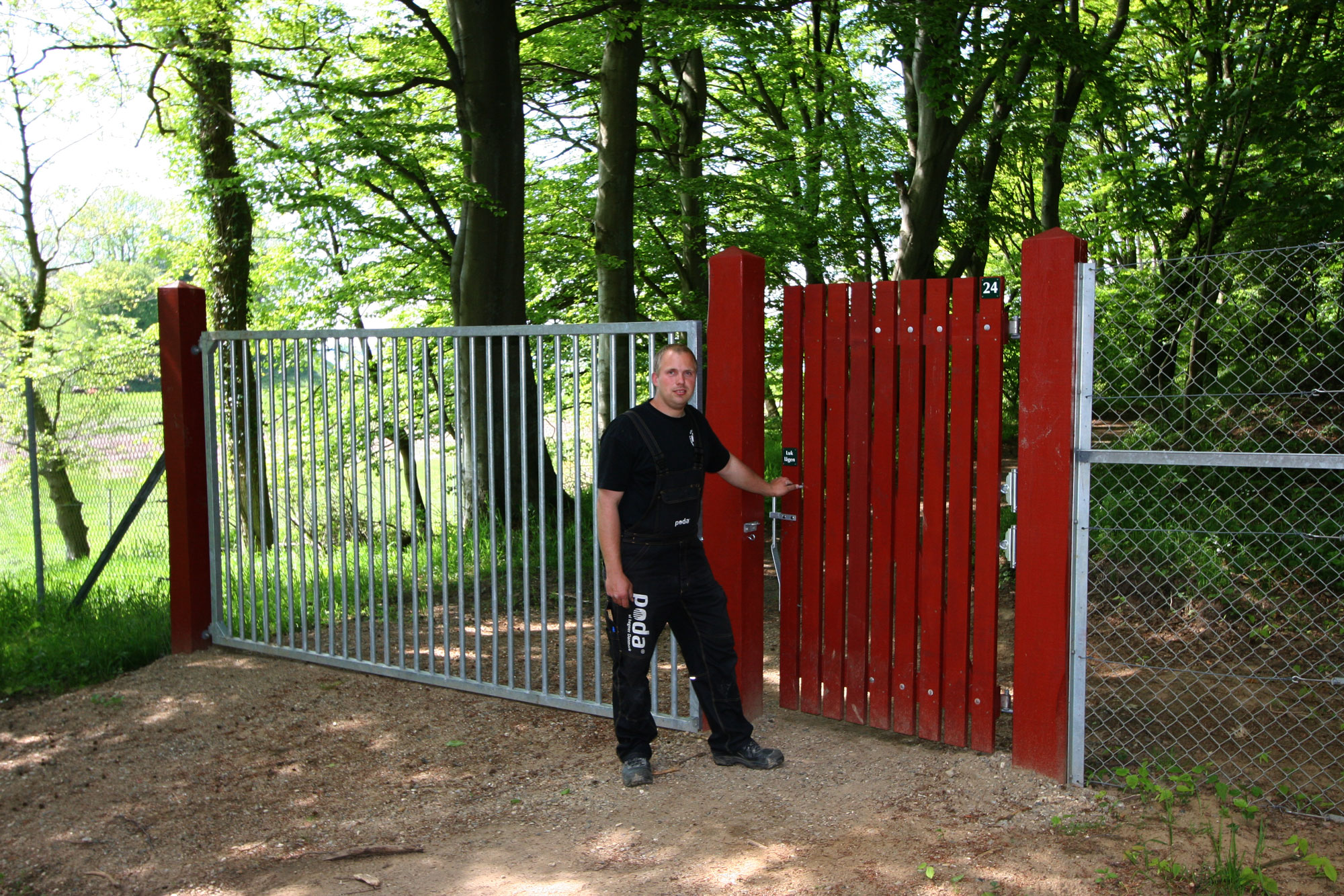 Ein Mann steht vor einem roten Holztor, das in einen Tiergarten führt. Neben dem Tor befindet sich ein Stahltor.